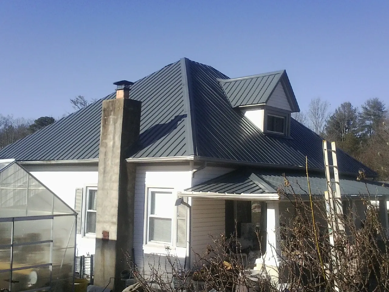 Dark blue standing seam metal roof on a white farmhouse with dormer — Slate & Tile Roof Repair by Roofing Brothers in Berryville