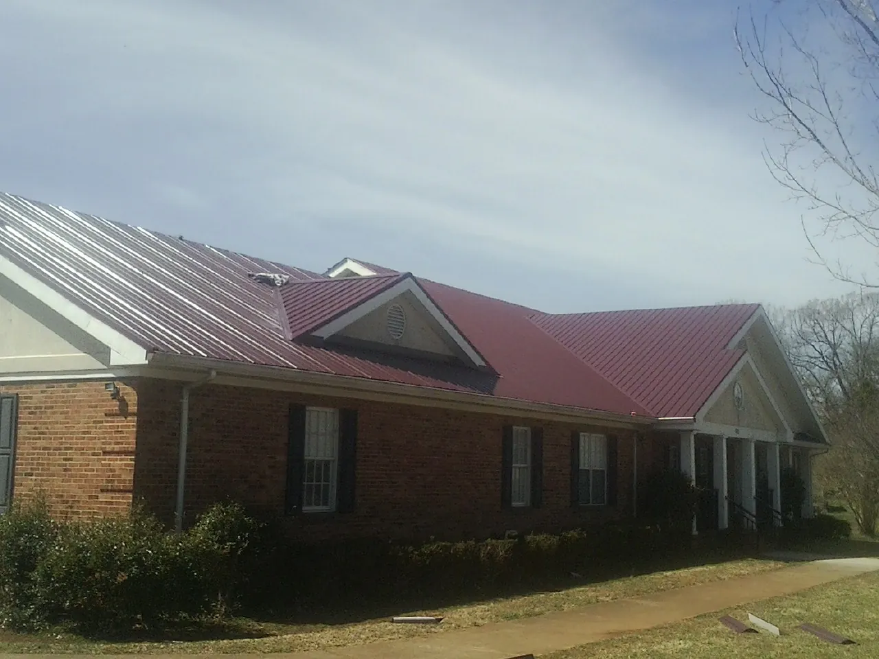 Red metal roof with gabled entries on a long brick building, from a Hail Damage Roof Repair job in Berryville