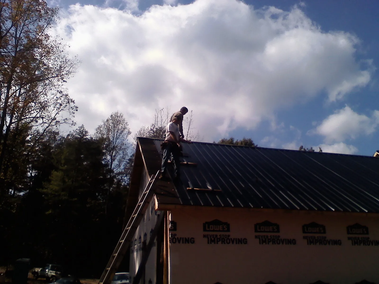 Roofer fastening dark metal panels high against a cloudy sky, from a Roof Inspection job in Berryville