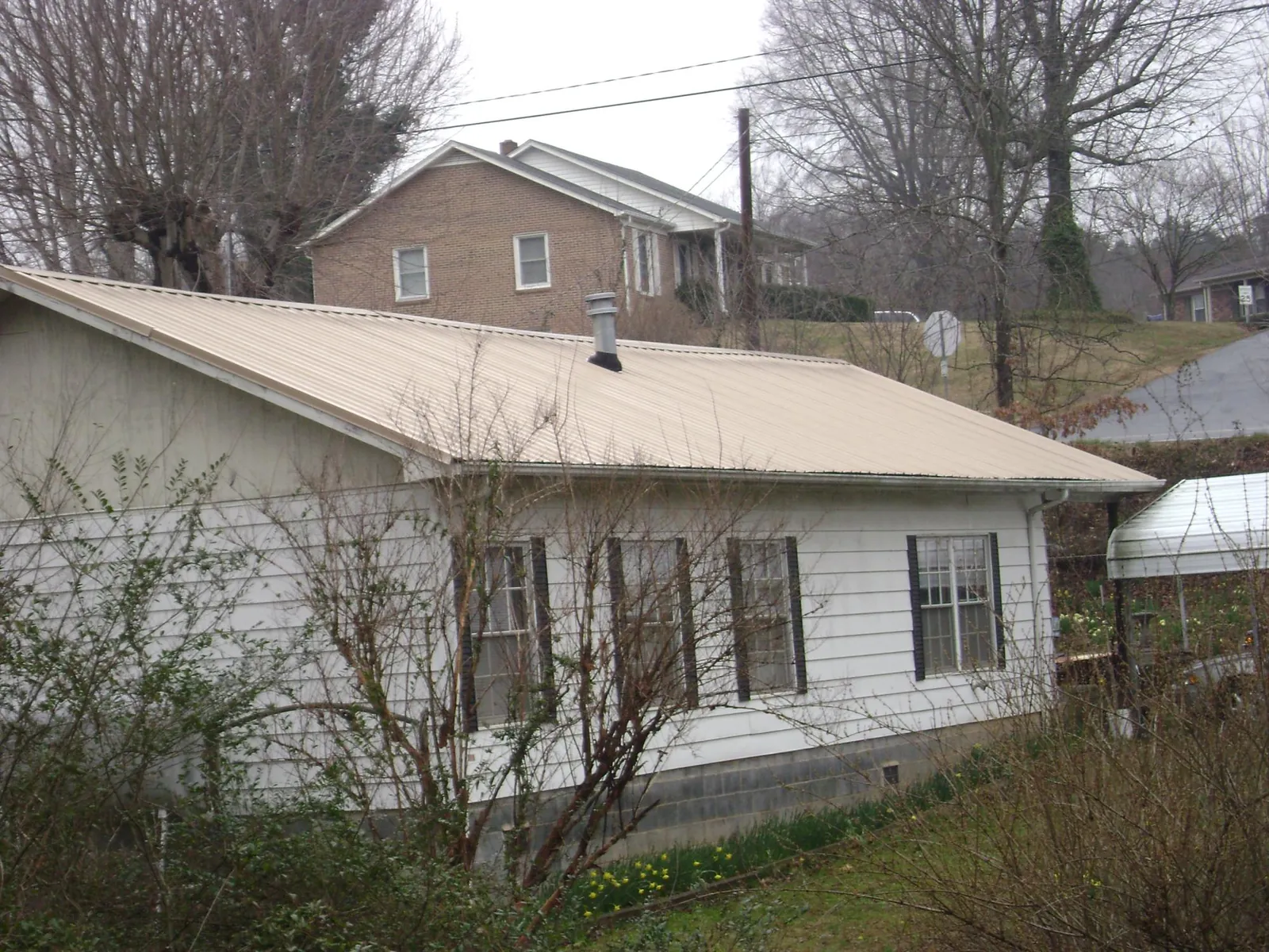 Tan metal roof on a white sided house set into a hillside — Commercial Roofing by Roofing Brothers in Berryville